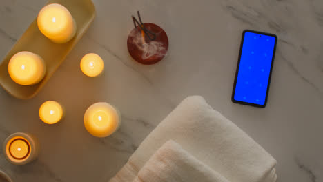 Overhead-View-Looking-Down-On-Still-Life-Of-Blue-Screen-Mobile-Phone-With-Lit-Candles-Towels-And-Incense-Stick-As-Part-Of-Relaxing-Spa-Day-Decor